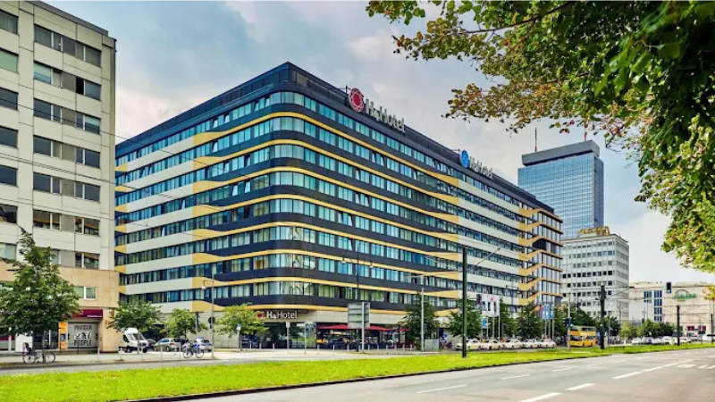 Fasad av H4 Hotel Berlin vid Alexanderplatz med modern glasbyggnad, flera v�ningar och centralt l�ge n�ra stadens sev�rdheter